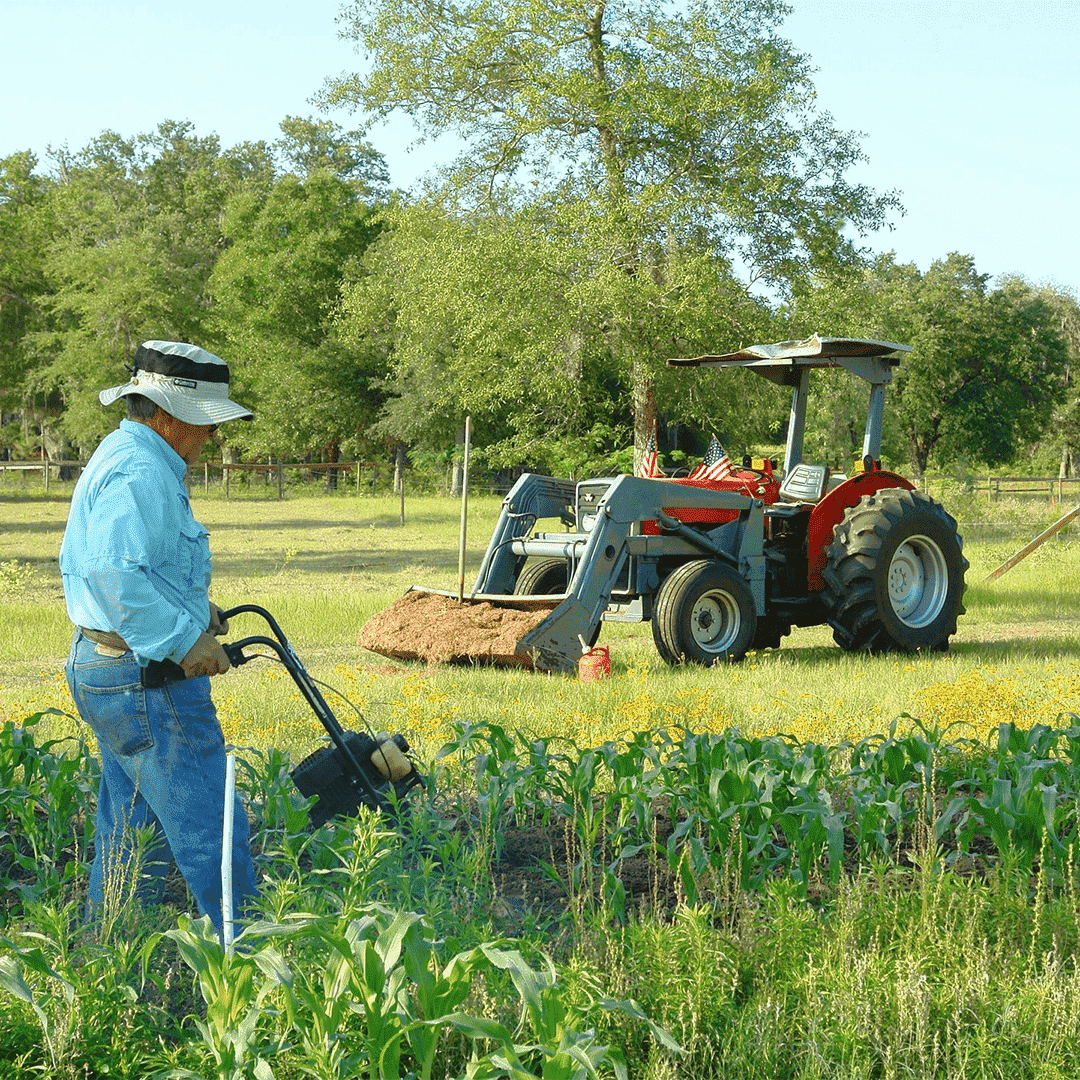 Agricultor utilizando una herramienta de cultivo en un campo verde cercano a un tractor 